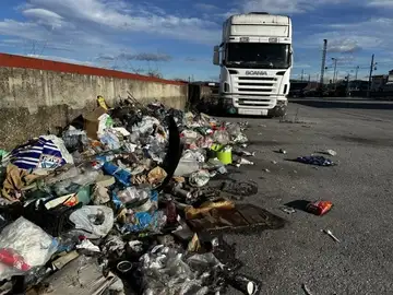 Velik kup odpadkov odvržen ob parkiranem tovornjaku pri betonskem zidu