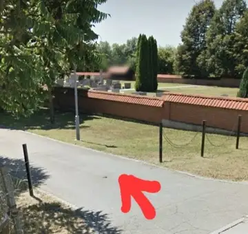 Razpokan pločnik z rdečo puščico, ki označuje poškodbo ob pokopališkem zidu
