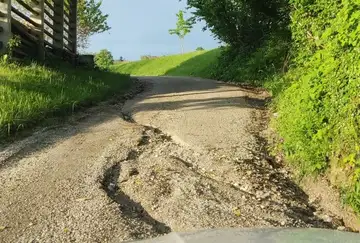 Poškodovana makadamska cesta z globokimi kolesnicami in erozijo