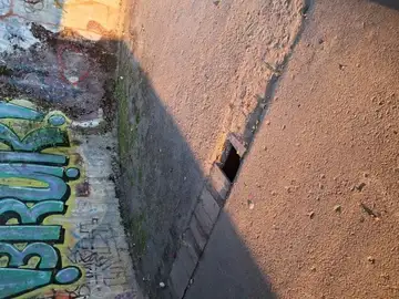 Odprt odtočni jašek na pločniku ob steni z grafiti