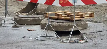 Odprt pokrov jaška z gradbenimi ovirami in paletami na cesti