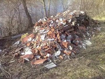 Kup gradbenih odpadkov odložen v naravi ob drevesih