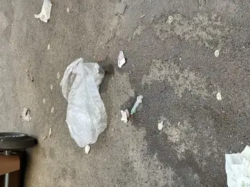 Plastična vrečka in manjši odpadki na asfaltu ob parkiranem avtu