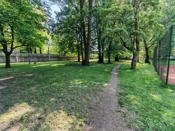Zdelana pešpot skozi travnat park z drevesi in teniškim igriščem