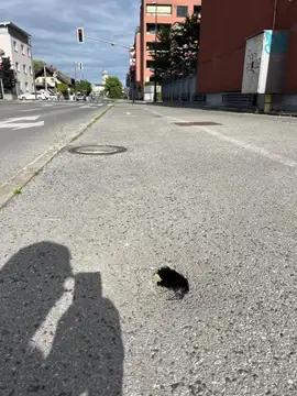 Luknja v pločniku pri semaforju in stavbah
