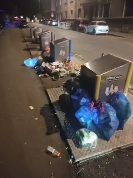 Prepolni koši za smeti z vrečami in smetmi na pločniku ponoči
