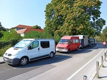 Več kombijev parkiranih ob cesti s kolesarjem