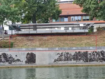 Betonski zid z odpadlim barvo ob vodi in travnatem pobočju